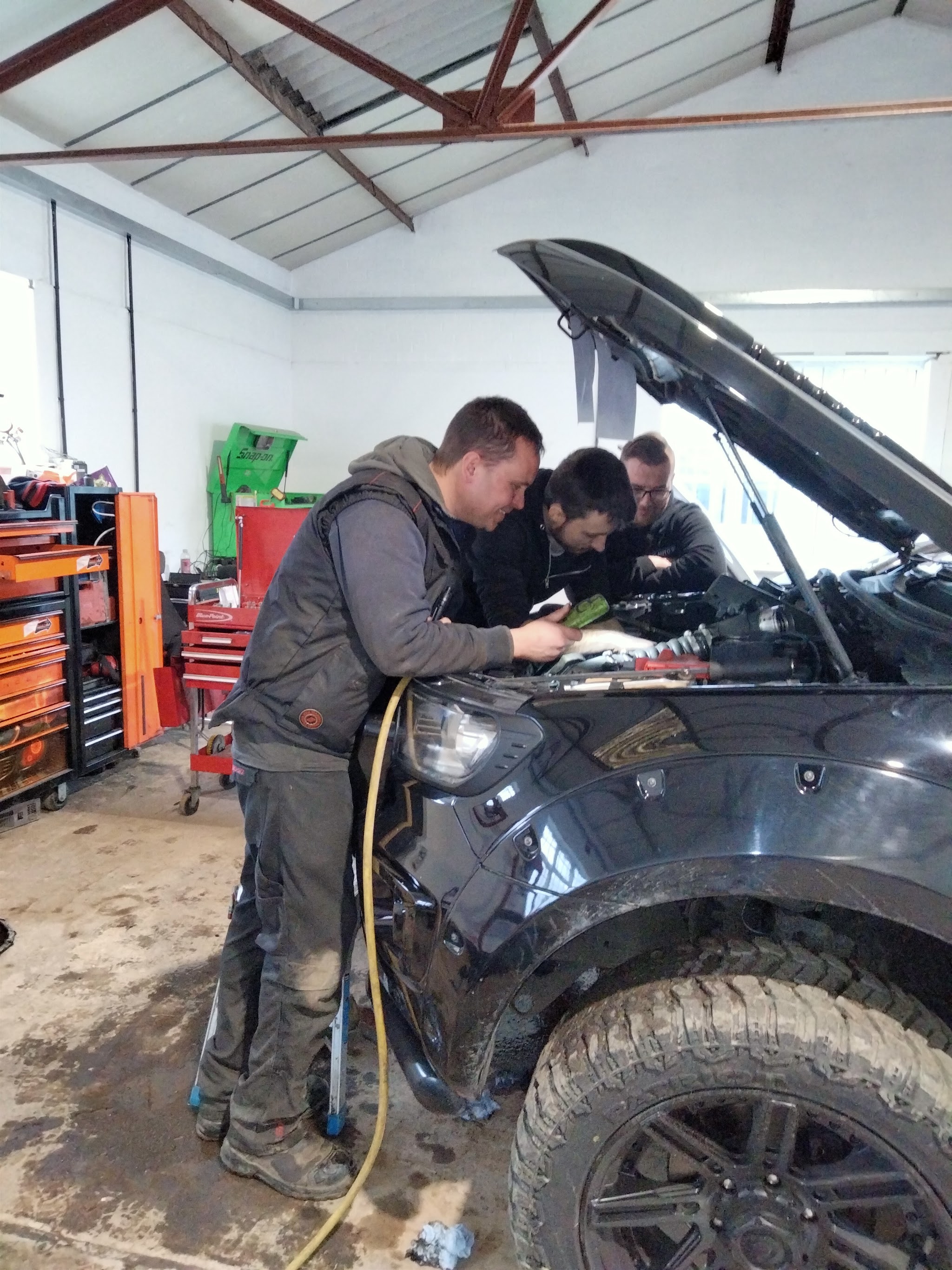 Three mechanics working under the bonnet of a black 4x4 in the workshop